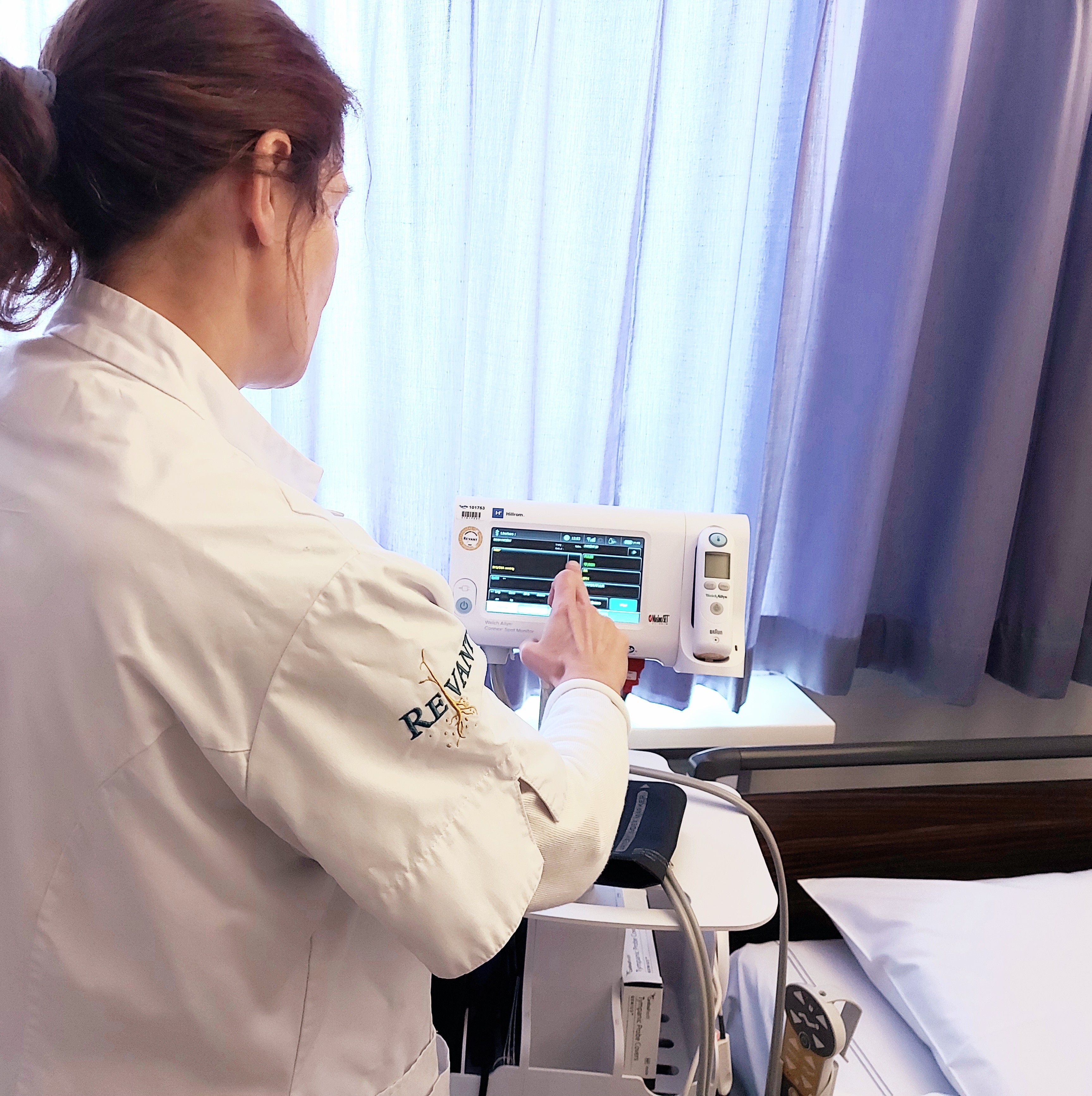 A woman wearing a white coat operates a medical device that displays multiple data points on a digital screen.